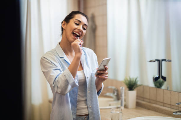 istock Happy woman texting on smart phone while brushing teeth in the morning. 1208515327