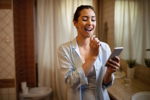 istock Young woman brushing teeth while reading text message on smart phone. 1208515419