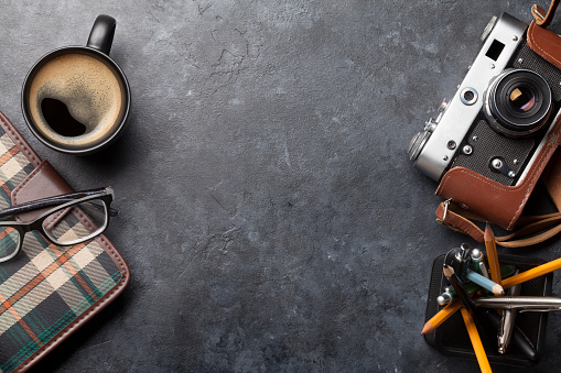 Office desk table with notepad, camera, supplies and coffee. Dark workspace tabletop with copy space. Top view flat lay