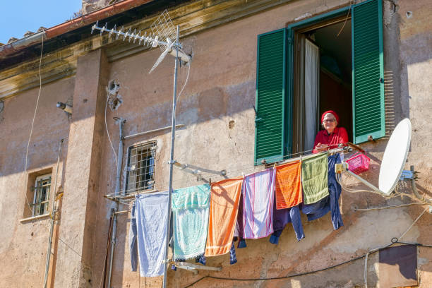 una donna anziana che guarda fuori dalla finestra di una casa nel quartiere garbatella nel quartiere ostiense di roma - balcony rome window ornate foto e immagini stock