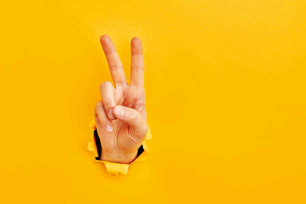 Human hand reaching through torn yellow paper sheet showing number two