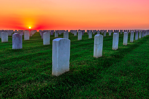 National cemetery with rows of white gravestones. The sunset sun above the ocean in San Diego Bay at Point Loma, California, United States.