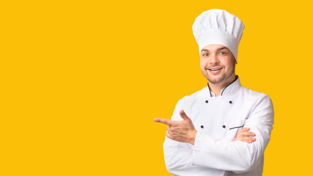 istock Male Chef Pointing Fingers Aside Standing On Yellow Background, Panorama 1208522535