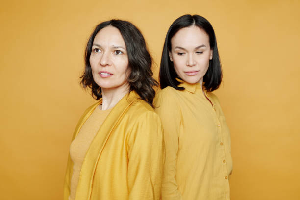 istock Asian adult daughter having difficult relationship with mother standing back to back with her against yellow background 1208523715
