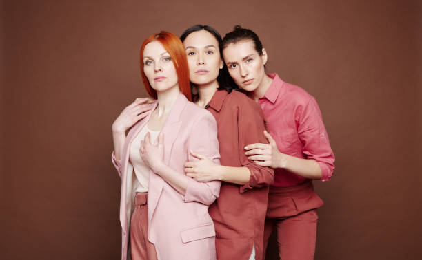 istock Three young multi-ethnic women with different appearances holding arms of each other against brown background 1208524760