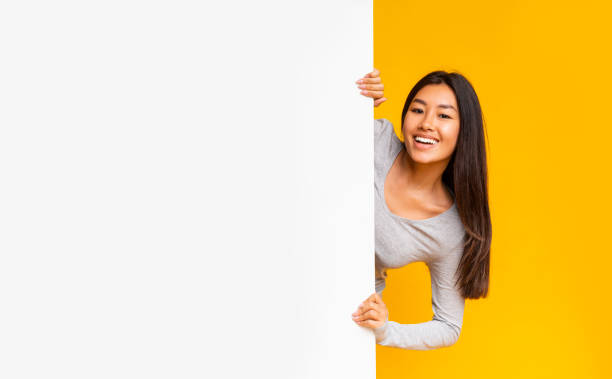 ładna azjatycka dziewczyna patrząca zza białej tablicy reklamowej - commercial sign marketing sign women zdjęcia i obrazy z banku zdjęć