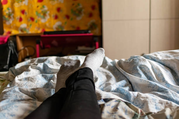 Thin female legs and feet in black pants and gray socks lie on the bed among colored fabric textiles stock photo