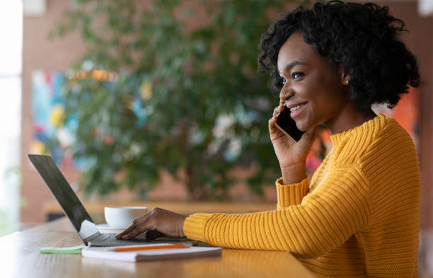 istock Smiling black girl talking to clients by phone, using laptop 1208530145