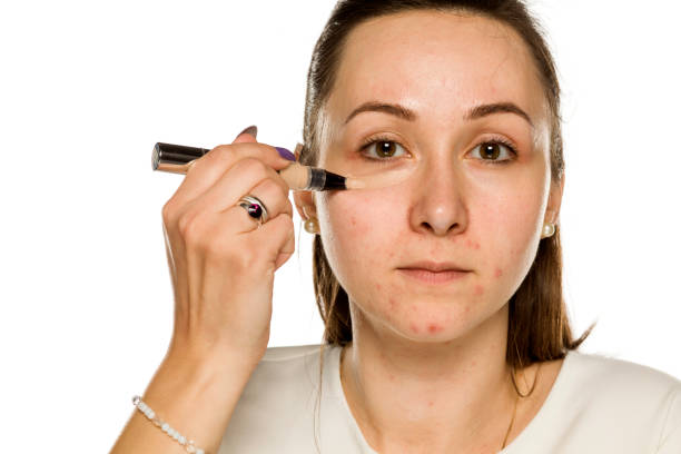 istock Young woman applying concealer on her face on white background 1208532533