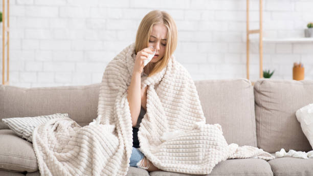istock Sick girl wrapped in blanket blowing nose 1208532613