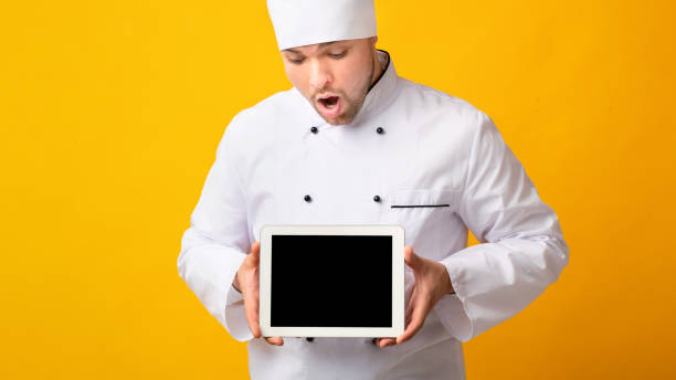 istock Excited Chef Looking At Tablet Screen Standing, Yellow Background, Mockup 1208532743