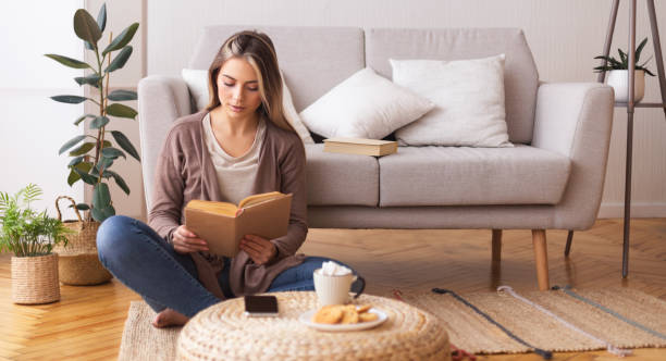 młoda kobieta czyta książkę, siedząca na podłodze w domu - book reading white women zdjęcia i obrazy z banku zdjęć