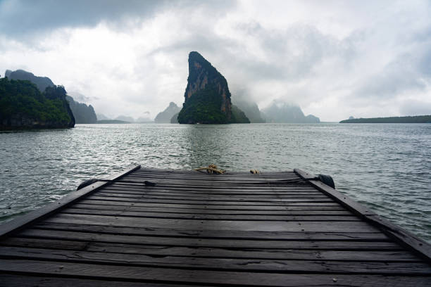 Wooden pier with cloudy sky and dark islands background at Koh Panyee island in Phang Nga, Thailand.