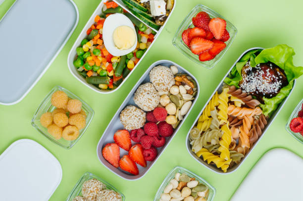 istock Pattern of plastic lunch boxes with healthy food on light green background 1208541756