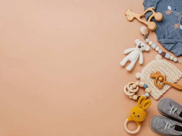 Newborn baby natural material accessories concept. Wooden toys, clothes and shoes on beige background with blank space for text. Top view, flat lay.