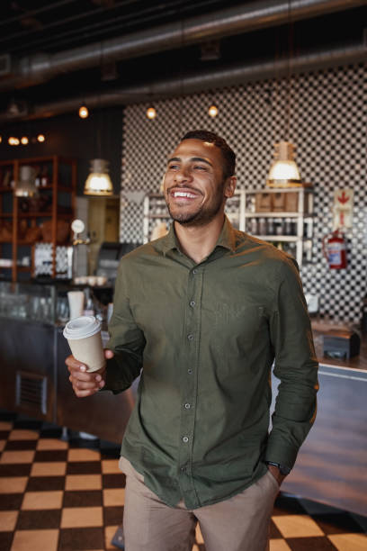 istock Handsome young afro-american man holding takeaway coffee mug standing in cafe 1208543438