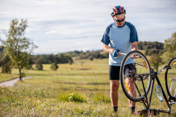 старший взрослый человек велосипедист надувая плоскую шину на своем велосипеде - фондовый фото - bicycle bicycle pump inflating tire стоковые фото и изображения
