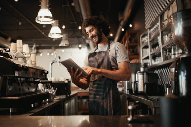 istock Cheerful young caucasian cafe owner wearing black striped apron using digital tablet 1208546682
