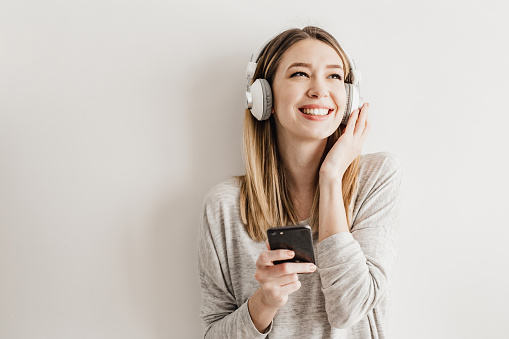 Smiling young  woman listening to music with headphones and mobile phone against isolated white background