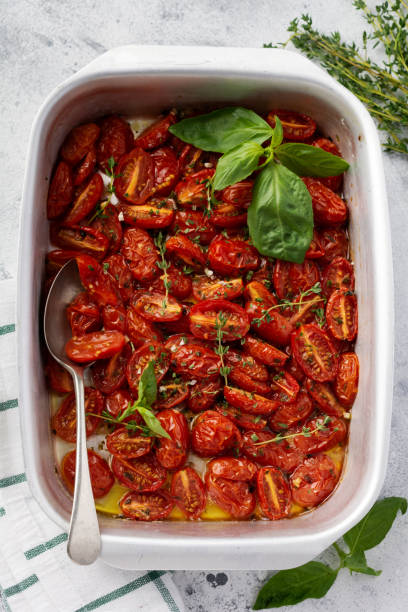 istock Baked cherry tomato with garlic, thyme and basil in old baking pan on concrete vintage background. Top view. 1208552498