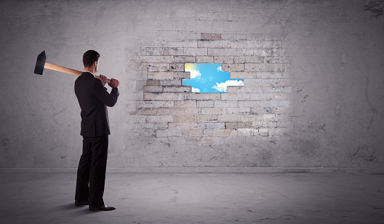 Business man hitting grungy brick wall with hammer