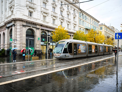 Nice, France - Nov 24, 2019: Traditional Nice tramway on a rainy day with pedestrians walking on Avenue Jean Medecin and BNP Paribas bank in background