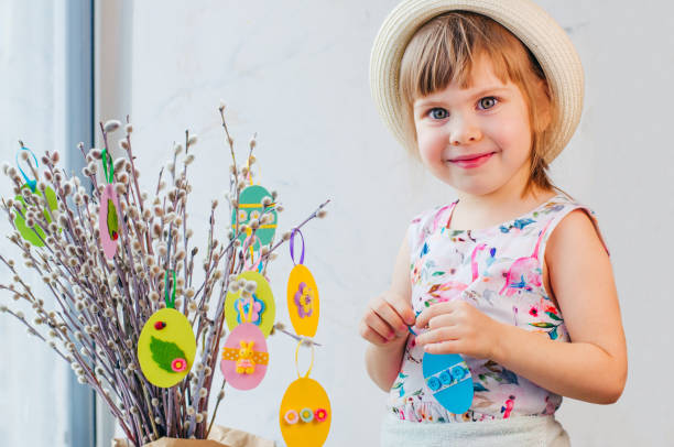 Beautiful little girl hanging Easter eggs cutted from color paper