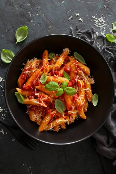 istock Penne pasta with tomato sauce, parmesan cheese and basil on dark backgound. 1208559284