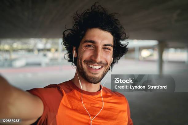 Portrait Of A Smiling Fit Young Man With Earphones In His Ears Taking Selfie Outdoors Pov Shot Of A Man Looking At The Camera Smiling Taking A Selfie Stock Photo - Download Image Now