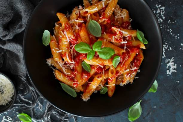 istock Penne pasta with tomato sauce, parmesan cheese and basil on dark backgound. 1208559350