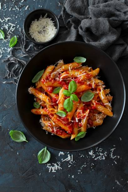 istock Penne pasta with tomato sauce, parmesan cheese and basil on dark backgound. 1208559384