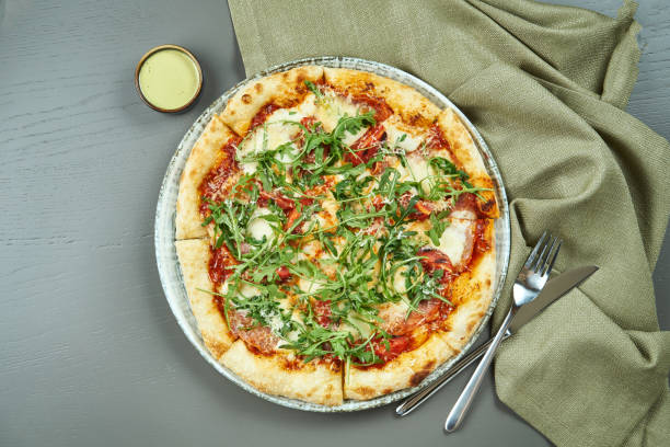 istock Top view on Appetizing pizza with prosciutto, arugula, tomatoes, parmesan and mozzarella on wooden background in a restaurant. Italian cuisine. 1208559503