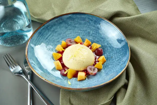 Photo of Panna Cotta - a delicious and beautiful dessert made of cream and vanilla with grapes and peach in a blue bowl on a wooden background. Italian cuisine