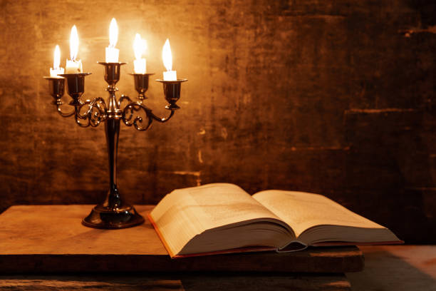 Open Holy Bible and candle on a old oak wooden table. Beautiful gold background. Religion concept.