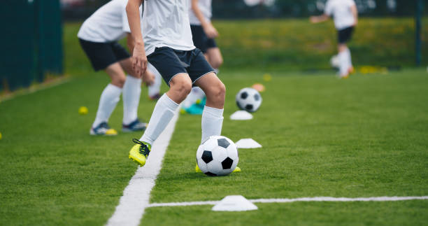 トレーニング中のスポーツサッカー選手。練習でサッカーボールを蹴る男の子。サッカーのピッチでサッカーをしている子供たち。ジュニアのための初心者サッカードリル - 練習 ストックフォトと画像