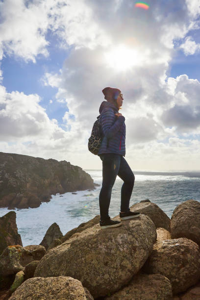 молодая женщина-туристка на мысе кабо-да-рока стоит на скалистом краю скалы. волны океана разбиваются о скалы на дне скалы - hiking coastline waters edge sunny стоковые фото и изображения