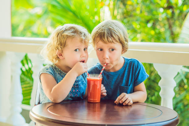 children boy and girl drink orange smoothie from papaya - cocktail orange cup juice imagens e fotografias de stock