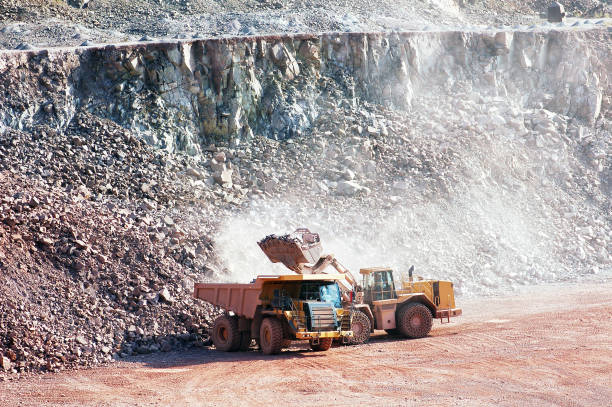 istock dumper truck gets loading on quarry with rock material by earth mover. mining. 1208567441