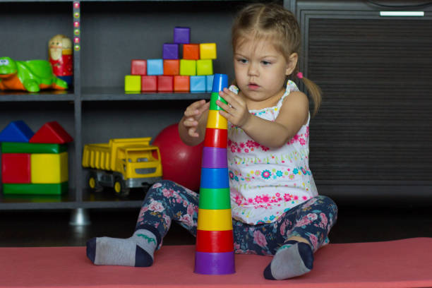 caucasian little girl of three years old building pyramid using colorful stacking cups - cup child geometric shape stacking imagens e fotografias de stock