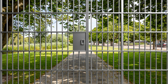 Privacy, no entry concept. View of a green park through a closed metal door with prison bars. The entrance is forbidden. 3d illustration