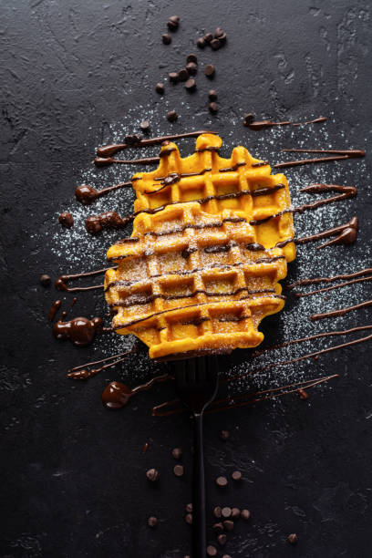 Pumpkin waffles with chocolate and sugar powder on dark old background. Top view