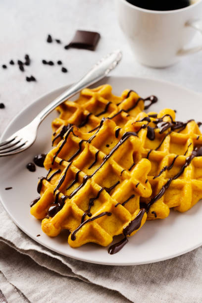 Pumpkin waffles with chocolate and icing sugar on light background and old rustic breakfast table. Top view.