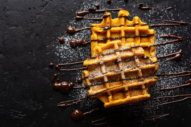 Pumpkin waffles with chocolate and sugar powder on dark old background. Top view
