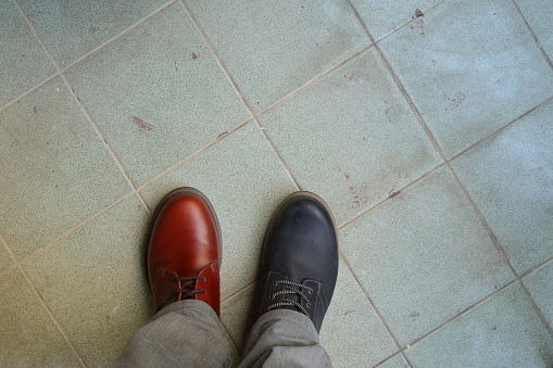 Closeup upper of mismatched shoes, a man wearing two different shoes and different colors standing on tiled floor, break the rules, revolution metaphor