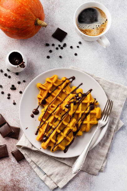 Pumpkin waffles with chocolate and icing sugar on light background and old rustic breakfast table. Top view.