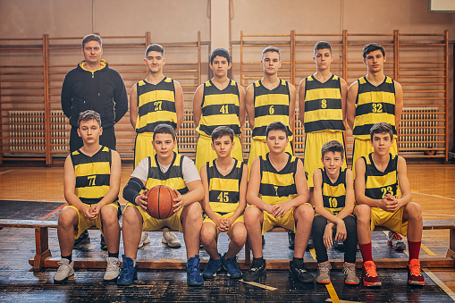 Group of men, group photo of teenage men basketball team and their coach.