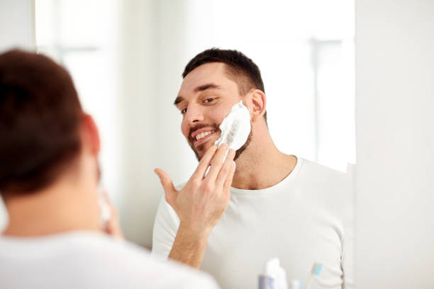 istock happy man applying shaving foam at bathroom mirror 1208570595