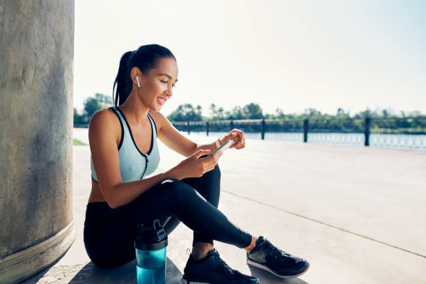 Happy fit woman holding smartphone and counts calories in sport app after running stock photo