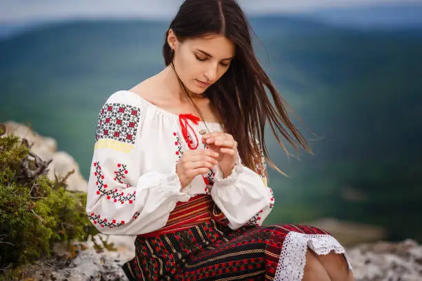 Photo of Attractive woman in traditional romanian costume on mountain green blurred background.