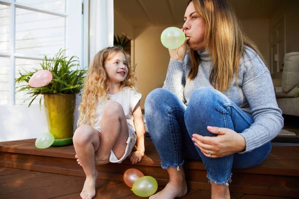 mamá haciendo estallar un globo para su linda hija pequeña - balloon blowing inflating child fotografías e imágenes de stock